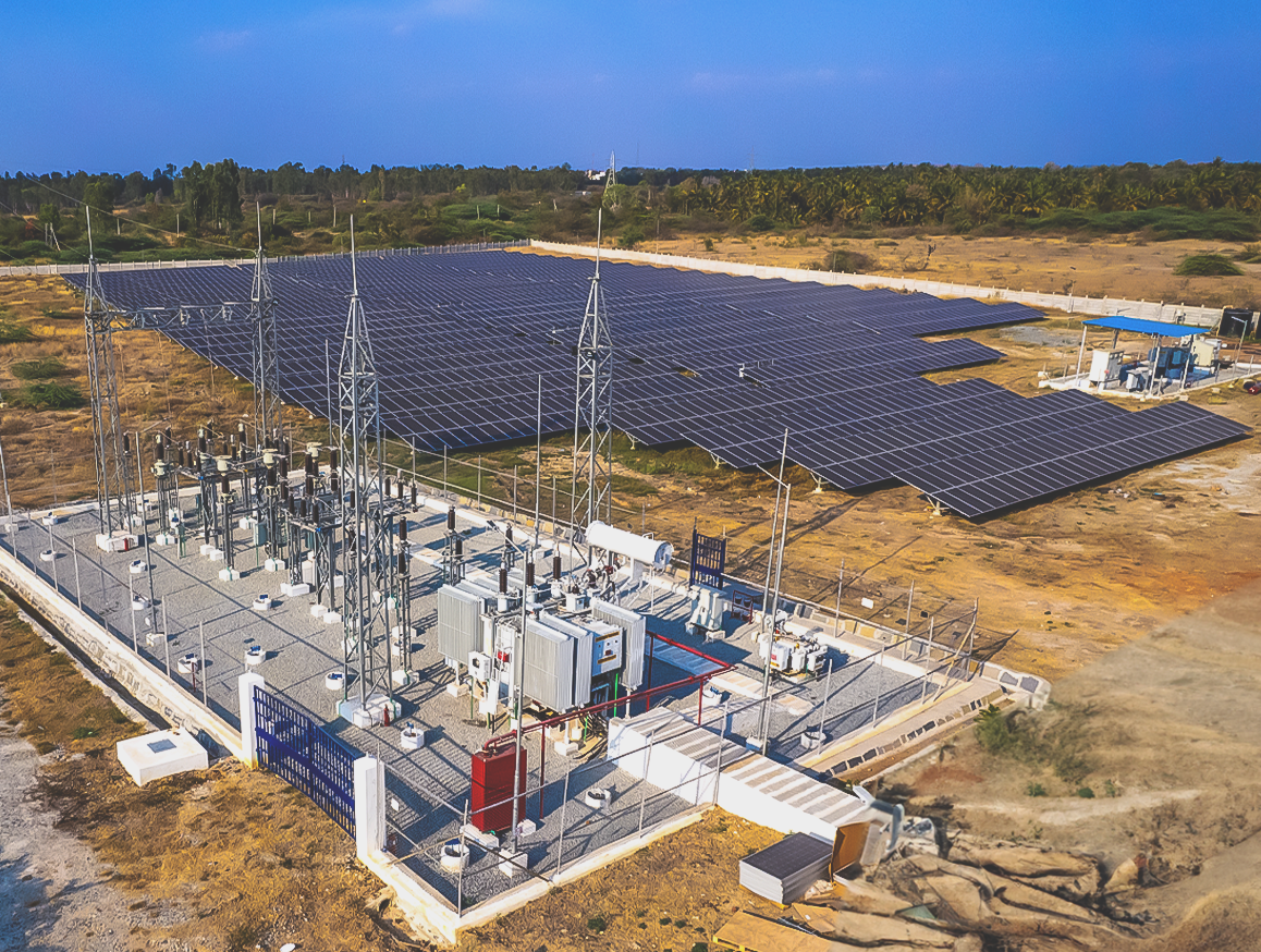 An aerial view of a ground mounted solar power plant with a substation, showcasing solar panels and electrical infrastructure.